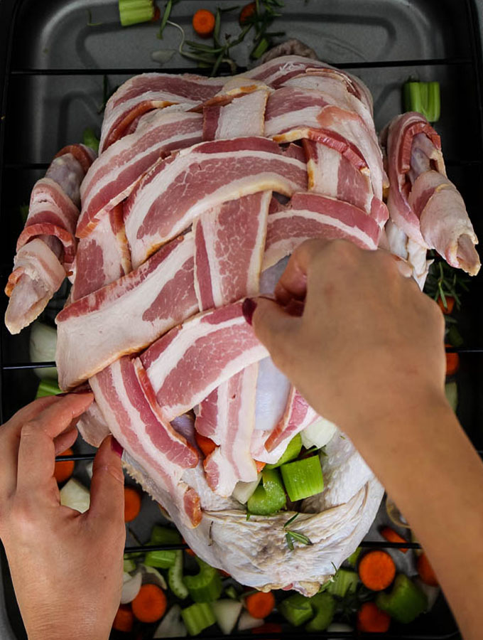 Bacon wrapped turkey is easy to make by stuffing the turkey cavity with carrots, celery, and onion, then applying a bacon weave on top of the turkey.