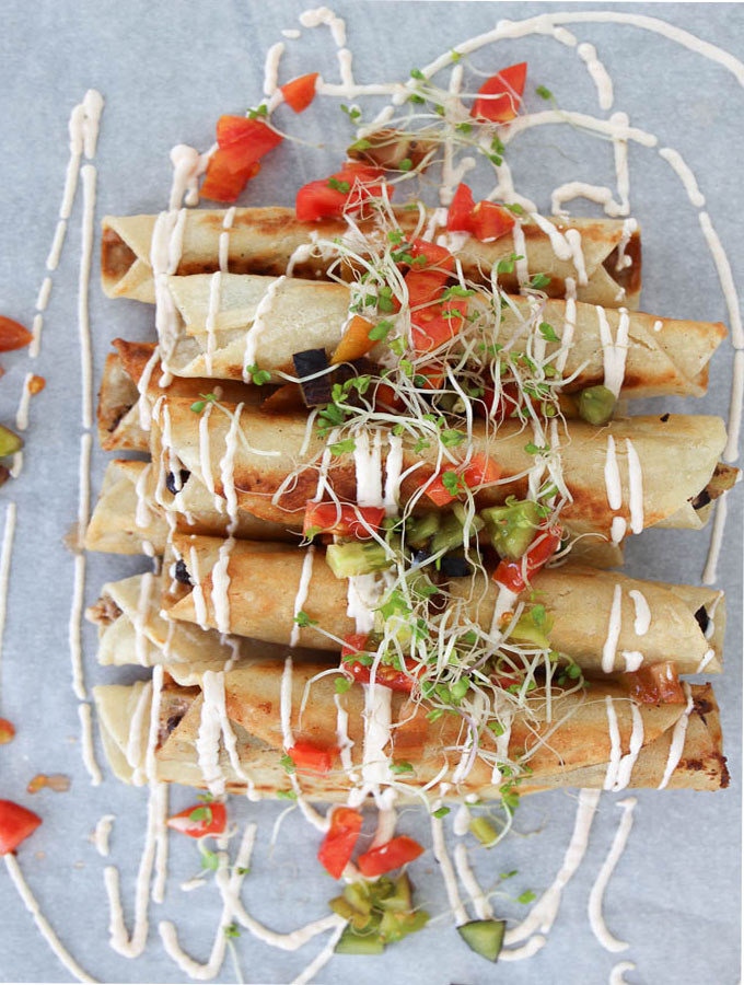 taquitos on a plate drizzled with crema