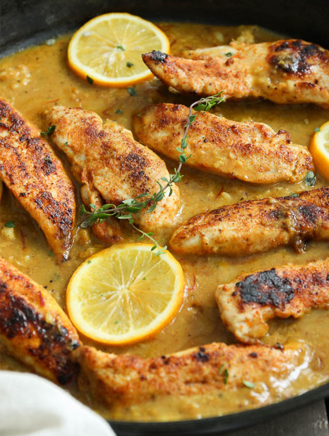 cooked chicken breasts in a skillet with sauce and lemon slices