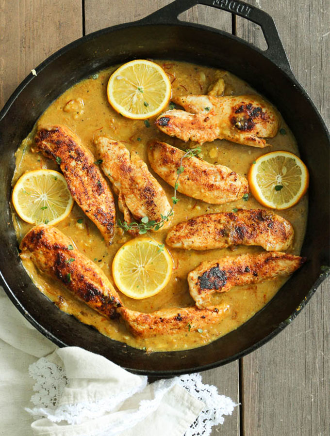 cooked chicken breasts in a skillet with sauce and lemon slices
