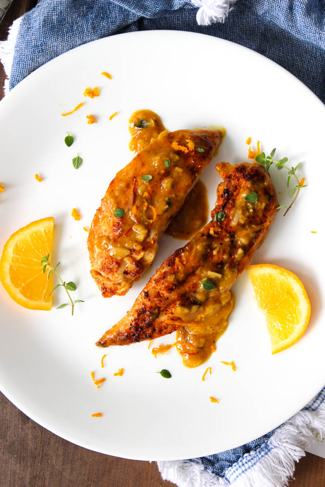 cooked chicken breasts on a plate with sauce and lemon slices