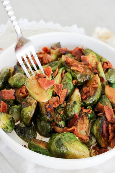 Pan roasted beer and bacon brussles sprouts, with a fork holding brussles sprout in a white bowl