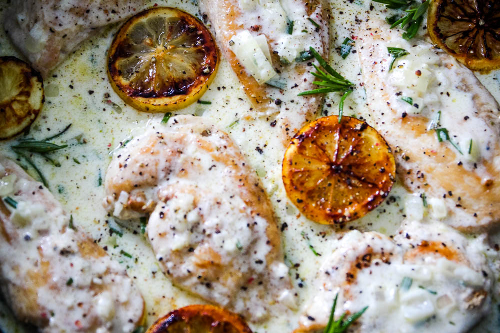 close up picture of One Pan Creamy lemon chicken in a black pan sprinkled with pepper.