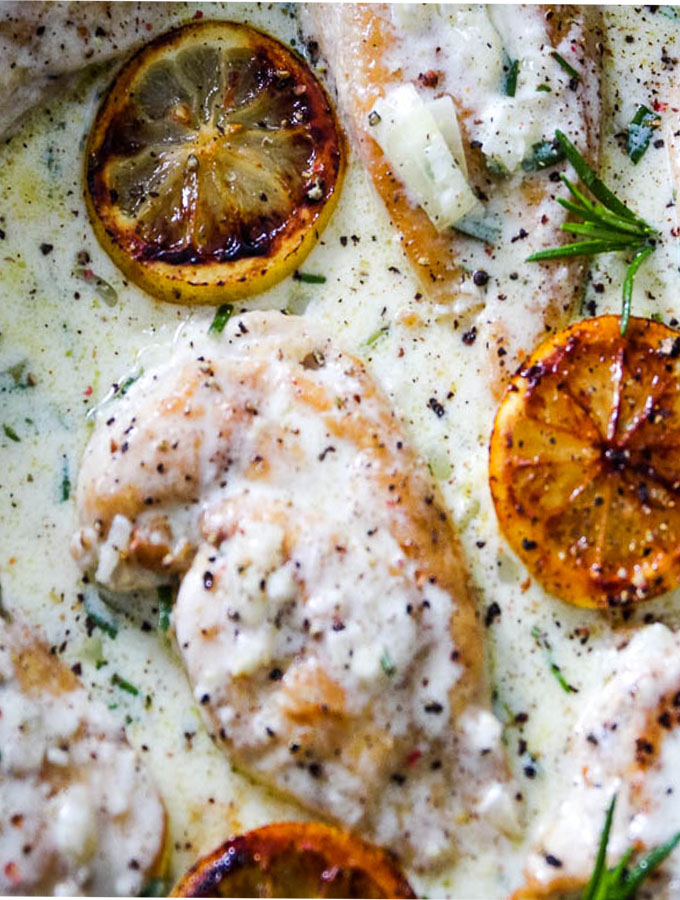 One Pan Creamy lemon chicken close up of a chicken filet in the lemon sauce and some charred lemons.