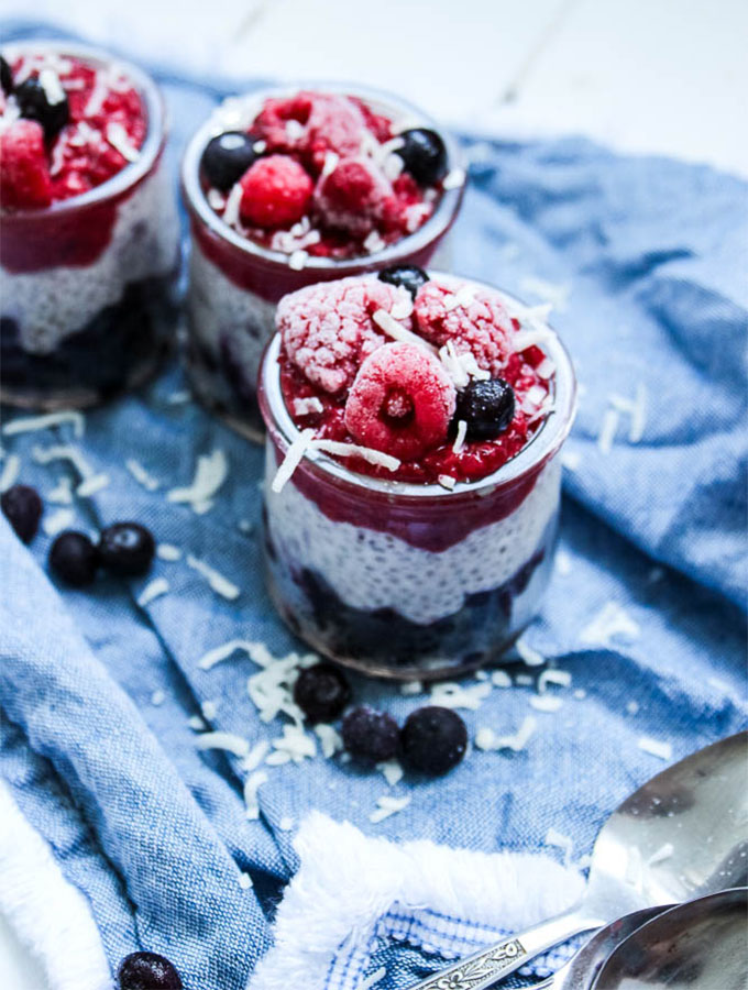 closeup shot of chia seed pudding topped with raspberries and blueberries in glass jars