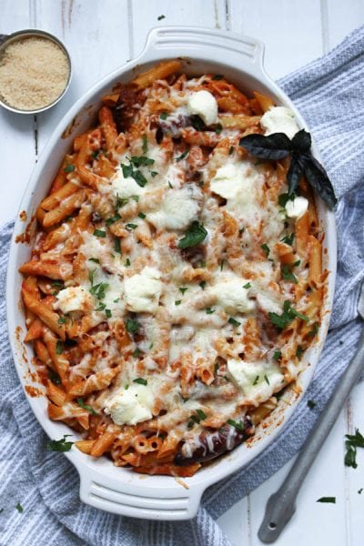 Baked penne pasta in a large dish with cheese, sausage, peppers, sauce, and ricotta.