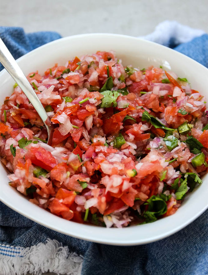 close up shot of pico de gallo with a spoon and white bowl