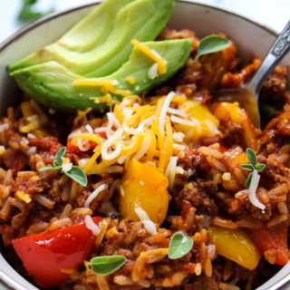 ustuffed bell pepper with ground beef skillet is plated with shredded cheese, avocado slices, and extra oregano in a white bowl.