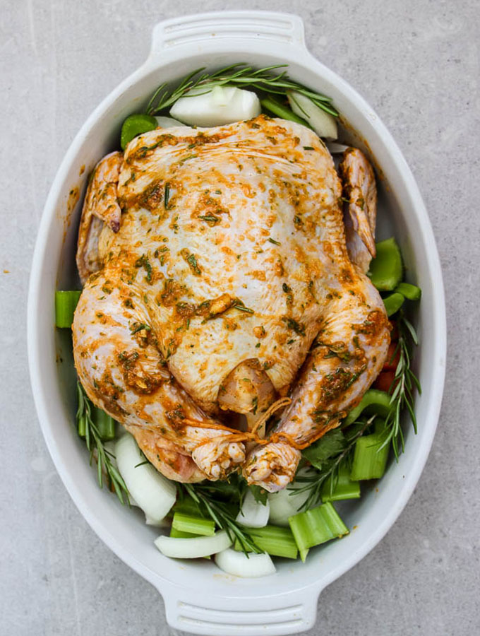 white wine and fresh herb roasted whole chicken is prepared and ready to go in the oven by stuffing the cavity and coating with a butter based marinade.