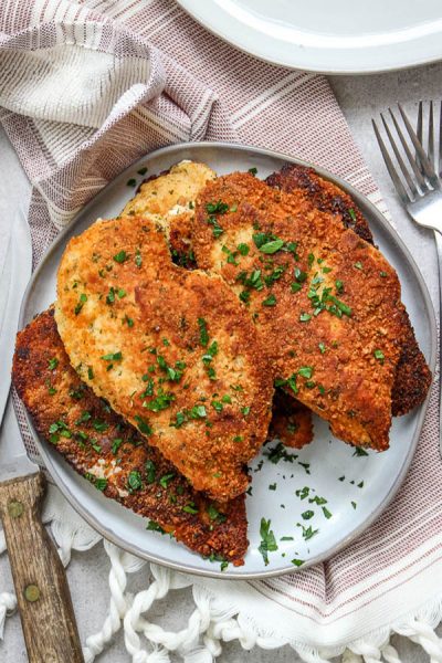 Parmesan cheese crusted chicken is plated with fresh parsley over a beautiful napkin.