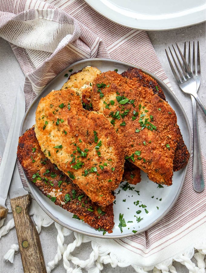 Parmesan cheese crusted chicken is plated with fresh parsley over a beautiful napkin.