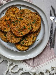 Crispy eggplant slices are plated on a gray plate with fresh parsley and a couple of forks.
