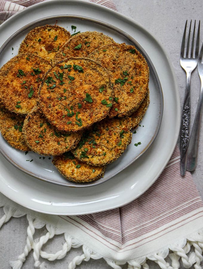 Crispy eggplant slices are plated on a gray plate with fresh parsley and a couple of forks.