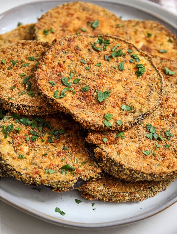Baked eggplant slices are plated on a white plate and topped with fresh parsley to show texture.