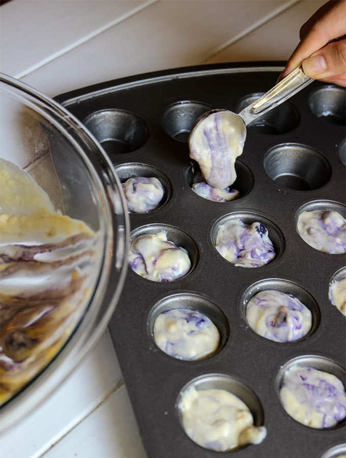 Blueberry mini pancakes being poured into the mini muffin pan with a tablespoon measurer.