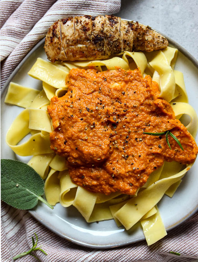 Pumpkin pasta sauce ontop of thick cut noodles and Italian chicken breasts is topped with freshly cracked pepper and fresh herbbs like rosemary and sage.