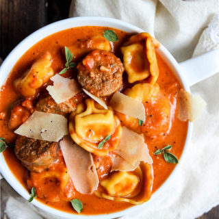 tortellini and sausage creamy tomato soup plated in a white bowl with a while towel.
