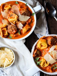 tortellini and sausage creamy tomato soup with a second bowl filled to the rim and a small cup of shaved parmesan cheese for delicious toppings.