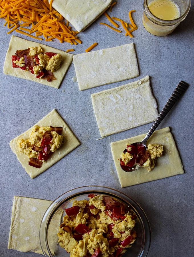Bacon, egg and cheese pop tarts are assembled by cutting squares in the dough, topping with the scrambled egg mixture, then topping with another square of dough.