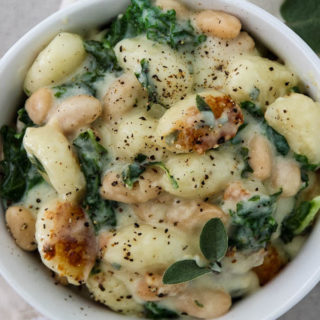 Creamy parmesan gnocchi with kale and white beans is plated in a white dish and topped with cracked pepper.