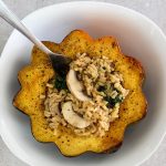 Stuffed acorn squash with rice, mushrooms and kale is plated in a white bowl with a fork.