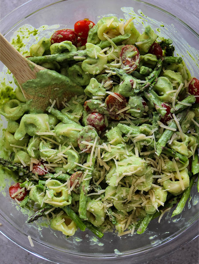 Green Goddess Tortellini Salad is mixed in a large glass bowl with a large wooden spoon.