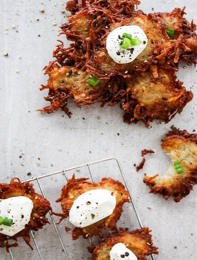 Potato latkes are stacked, then topped with a dallop of sour cream to show texture and crispiness.