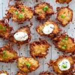Potato latkes are on a cooling rack and are topped with sour cream, chives, and cracked pepper.