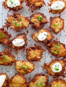 Potato latkes are on a cooling rack and are topped with sour cream, chives, and cracked pepper.