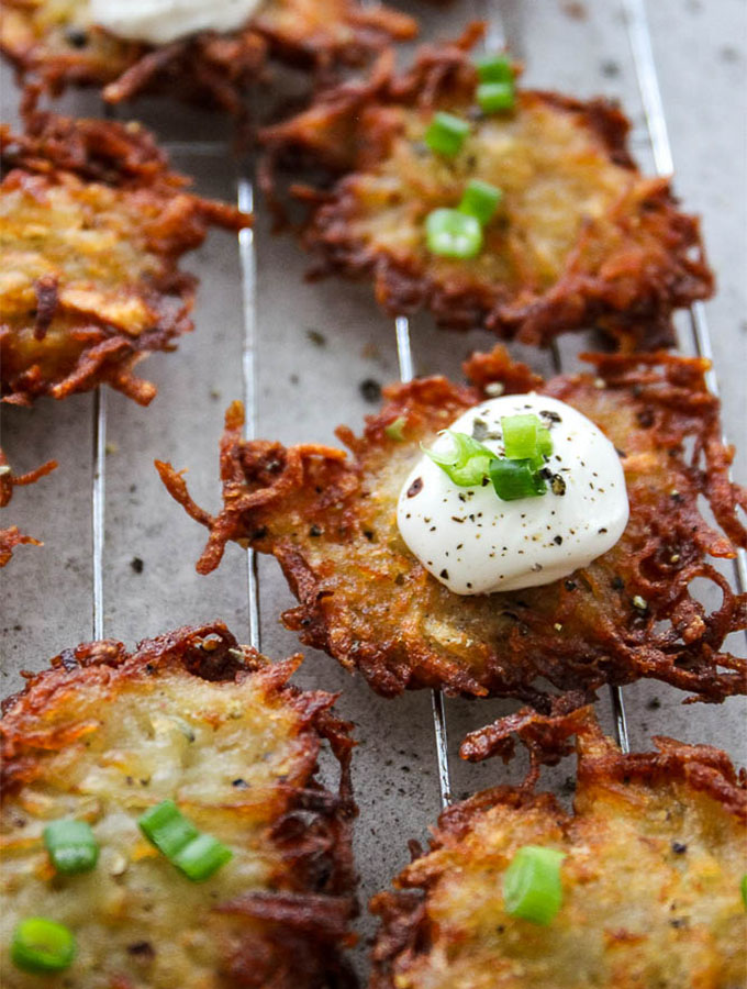 Potato latkes are topped with sour cream, chives, and fresh cracked pepper while they are on the cooling rack.