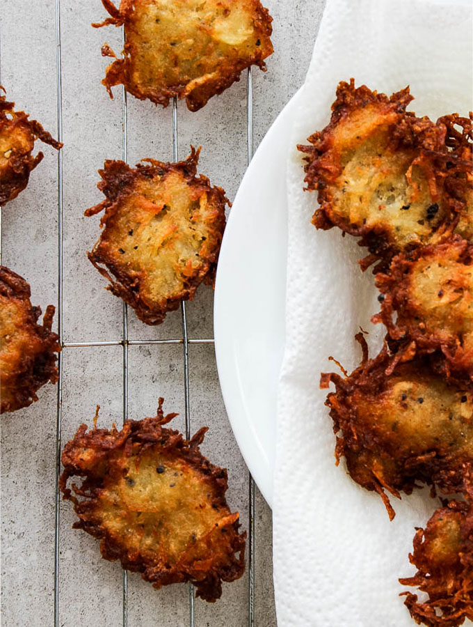 Potato latkes are plated on a cooling rack after resting on the paper towel.