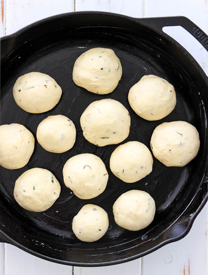 Rosemary Garlic Dinner Rolls are rolled into a ball and placed in a cast iron pan to get ready for baking.