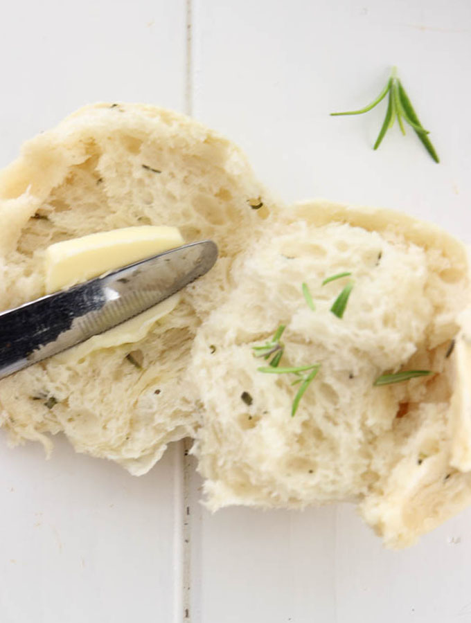 Rosemary garlic dinner bread rolls are halved and slathered with butter to show the airy and fluffy texture.