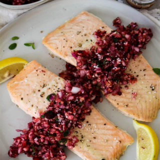 Salmon with Cranberry Relish is plated with heaps of relish on top of the salmon, wedges of lemon for added color, and course salt.