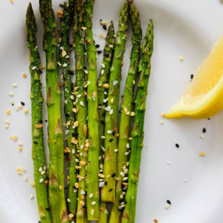 Asparagus is served on a white plate with lemon, and sprinkled with Trader Joe's Everything Bagel seasoning.