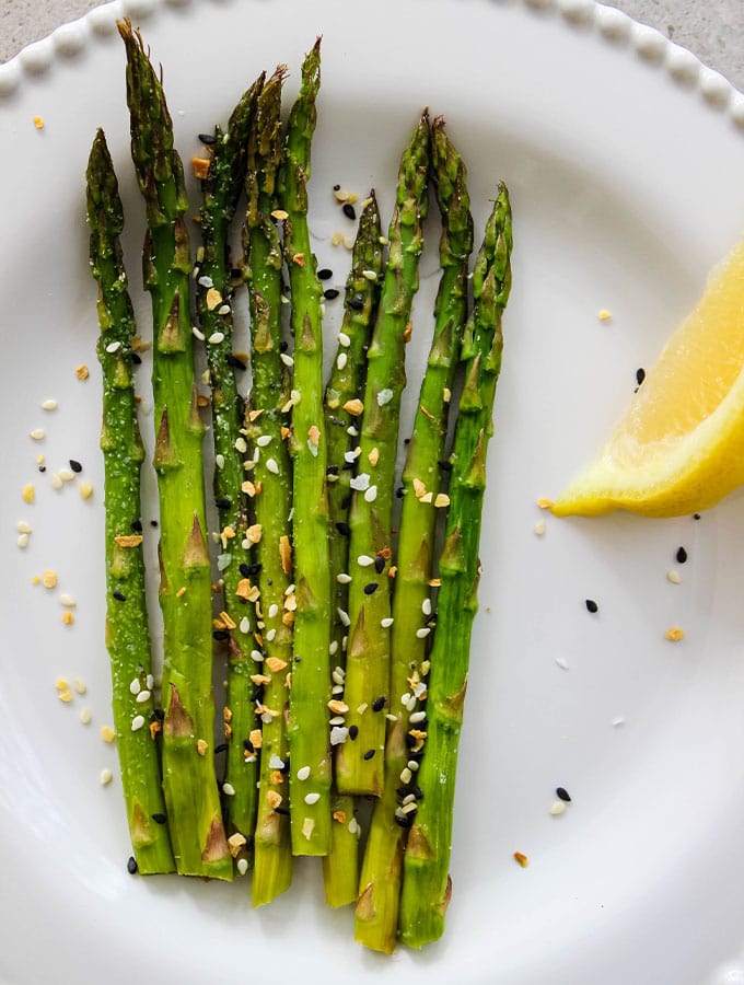 Asparagus is served on a white plate with lemon, and sprinkled with Trader Joe's Everything Bagel seasoning.