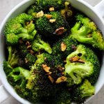 Pan roasted broccoli with garlic is plated in a white bowl and topped with the little bits of browned garlic.