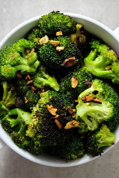 Pan roasted broccoli with garlic is plated in a white bowl and topped with the little bits of browned garlic.