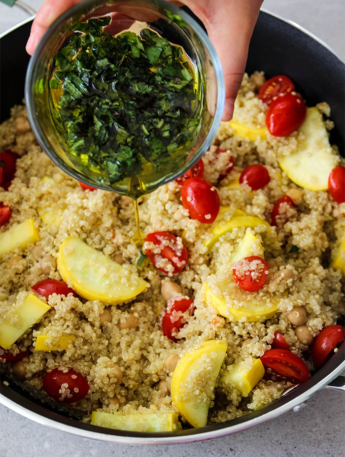 quinoa salad is in the pot and is topped with a olive oil, lemon juice and herb mixture.