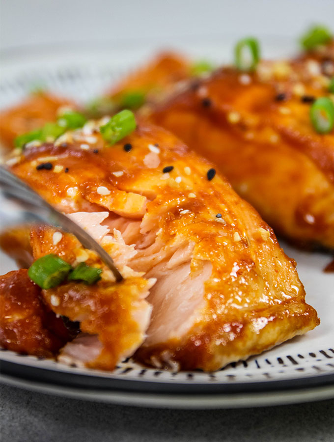 Sriracha Honey Baked Salmon is plated and flaked to show texture.
