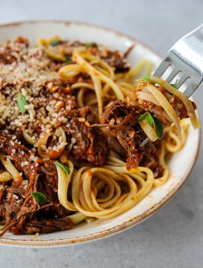 Instant Pot Beef Ragu Pasta is plated in a bowl, topped with cheese and fresh herbs.