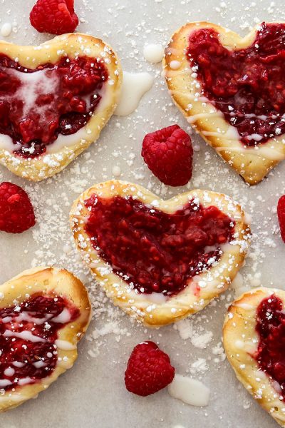 raspberry cream cheese puff pastry danish is frosted with icing and sprinkled with confectionary sugar.