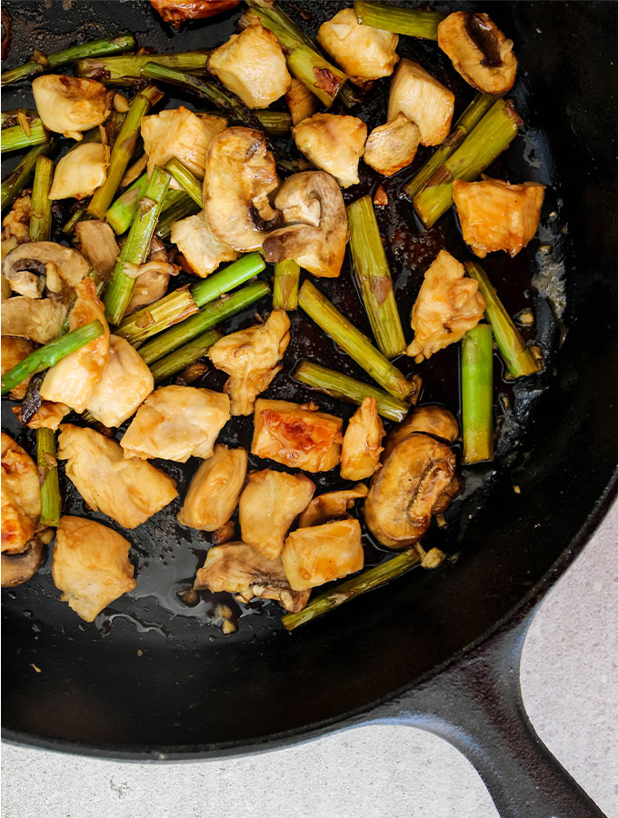 Honey garlic chicken stir fry is cooked on the stove top in a cast iron pan.
