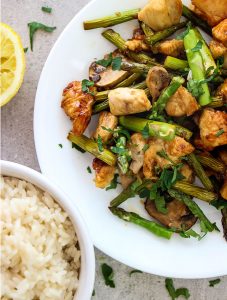 Honey garlic chicken stir fry is plated and served with rice and fresh parsley.