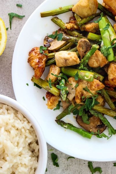 Honey garlic chicken stir fry is plated and served with rice and fresh parsley.