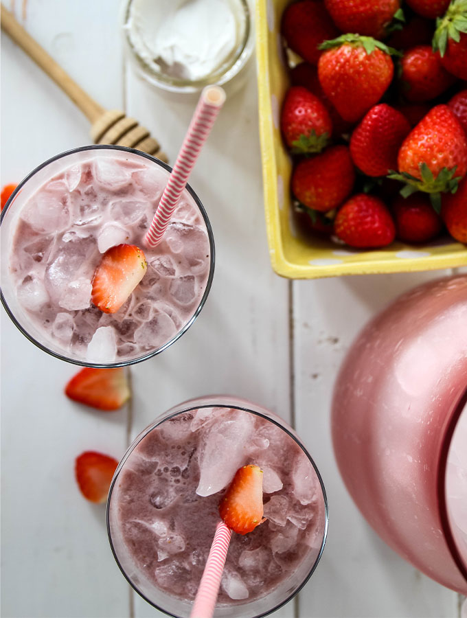 Pink drink is poured into two glasses and topped with strawberries.