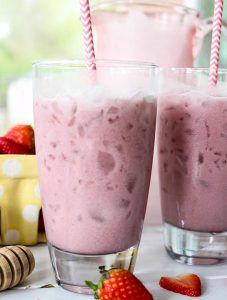 Pink drink is poured into two glasses and topped with straws and strawberries