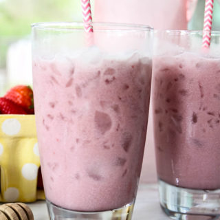 Pink drink is poured into two glasses and topped with straws and strawberries