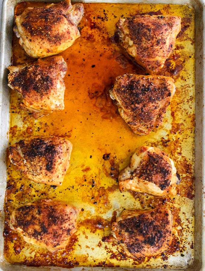 Chicken thighs are cooked in their juices on a sheet pan.