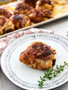 A chicken thigh is placed on a white plate with a sprig of thyme.